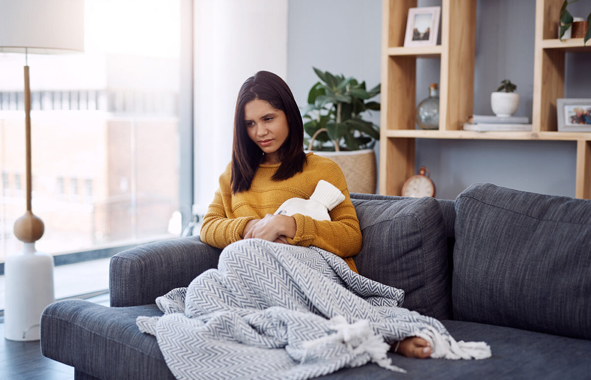 young woman suffering from stomach cramps while sitting on a sofa at home