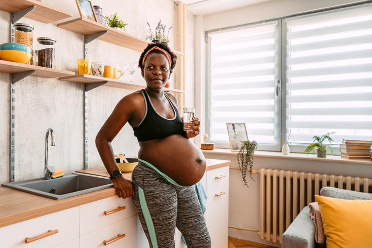 Beautiful black young pregnant woman drinking water after doing yoga at home.