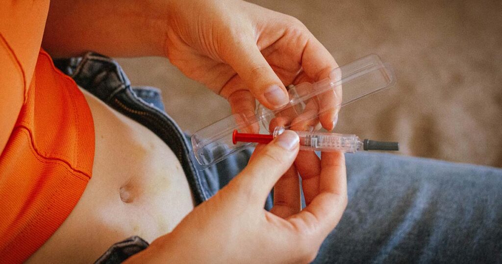 Woman holding syringe with stomach showing preparing to give herself a shot of hormones.